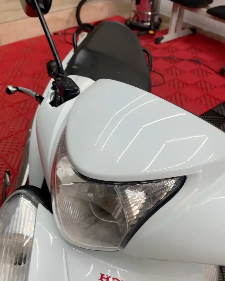 Detalhe do farol e da carenagem de uma moto branca no estúdio